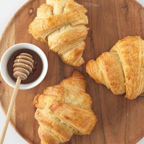 Croissants drizzled with honey and chocolate sauce on a white plate.