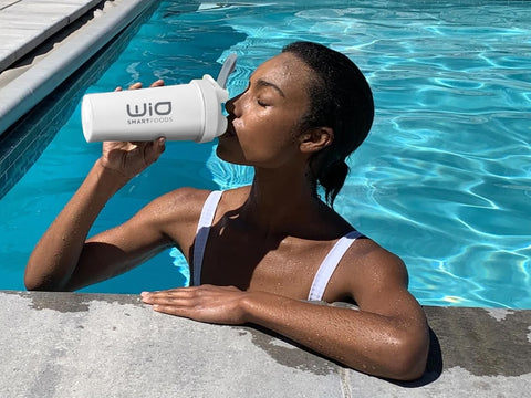 A girl enjoying a refreshing drink from a water bottle while relaxing in a pool.